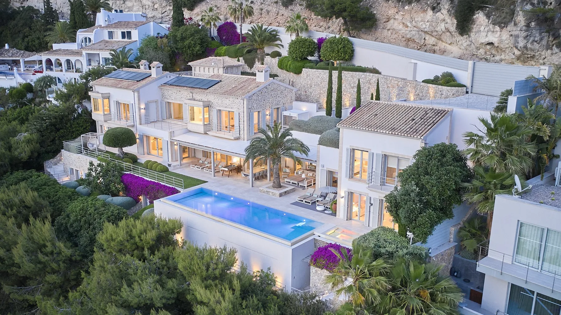A modern villa overlooks a rectangular swimming pool and landscaped gardens.