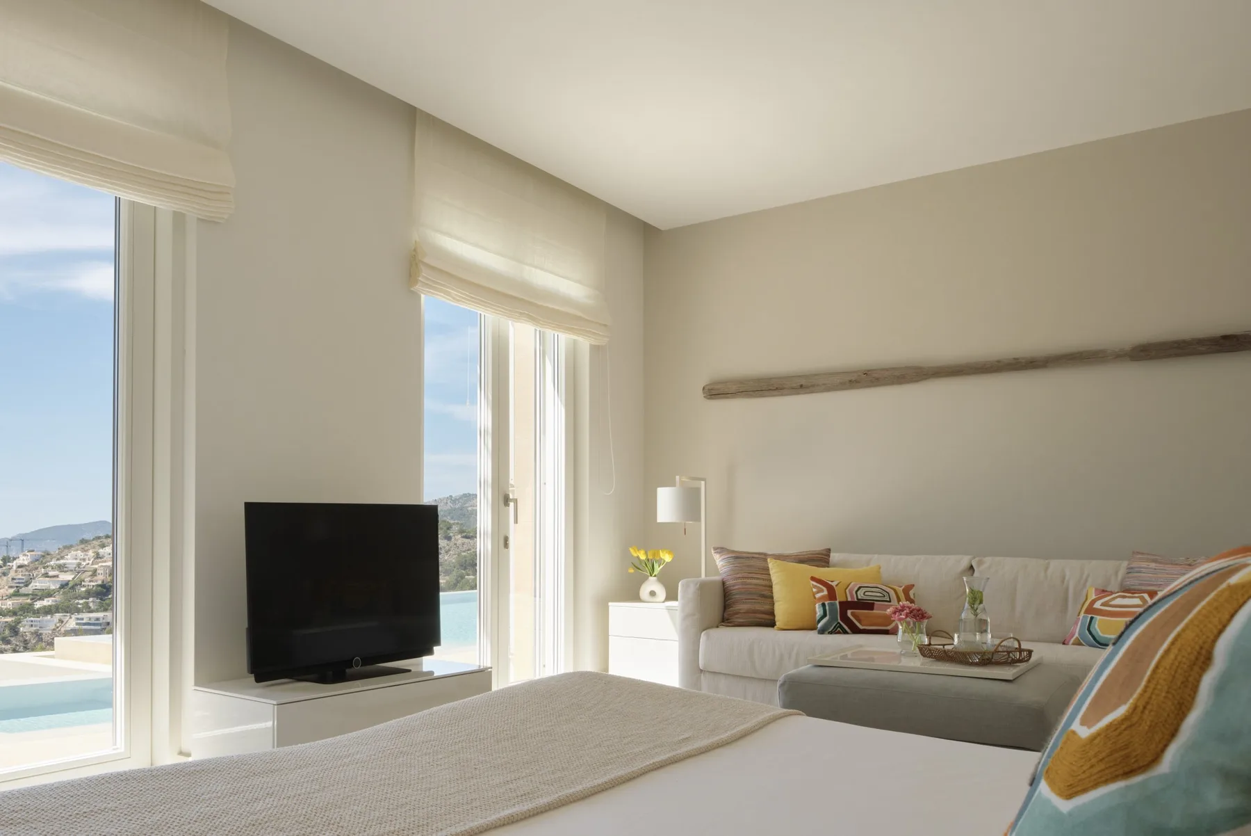 A bright bedroom with a bed, seating, and large windows overlooking the landscape.