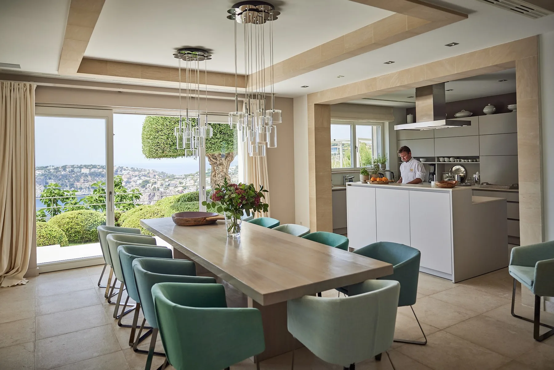 A dining area with a long table and green seating beside an open kitchen.