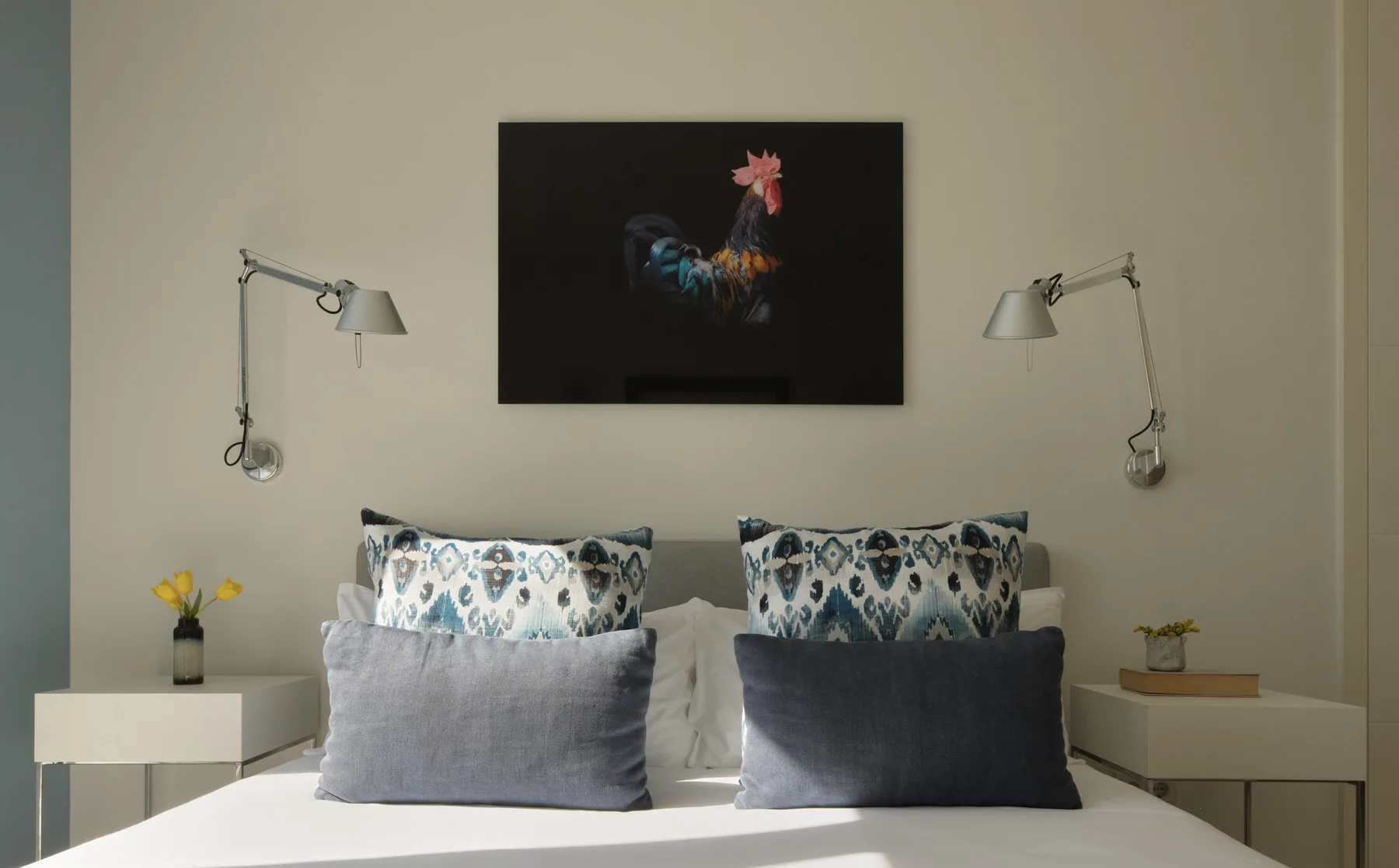 A bedroom with a bed, patterned pillows, and a framed artwork above it.