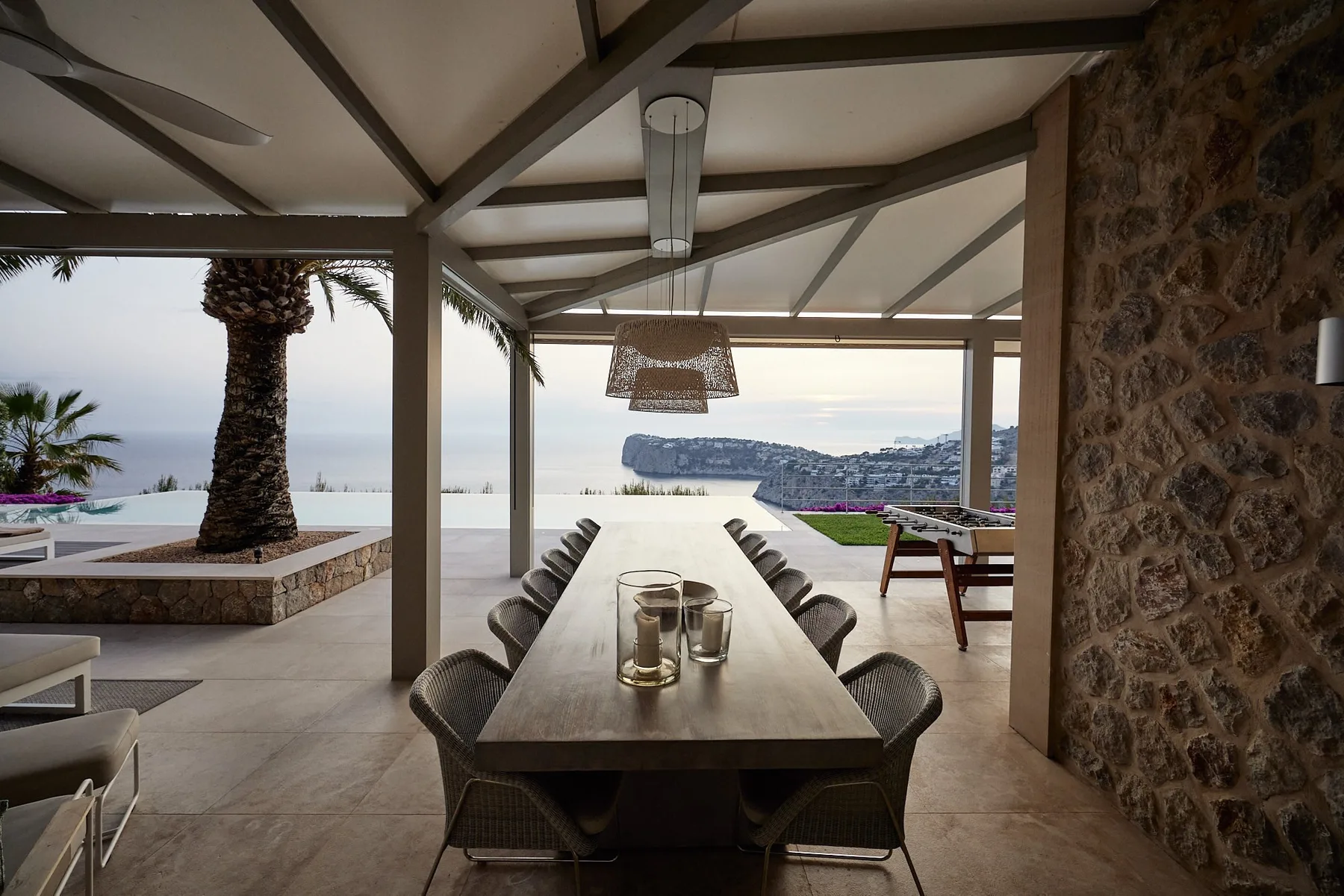 A covered outdoor dining area with a long table overlooking the sea.