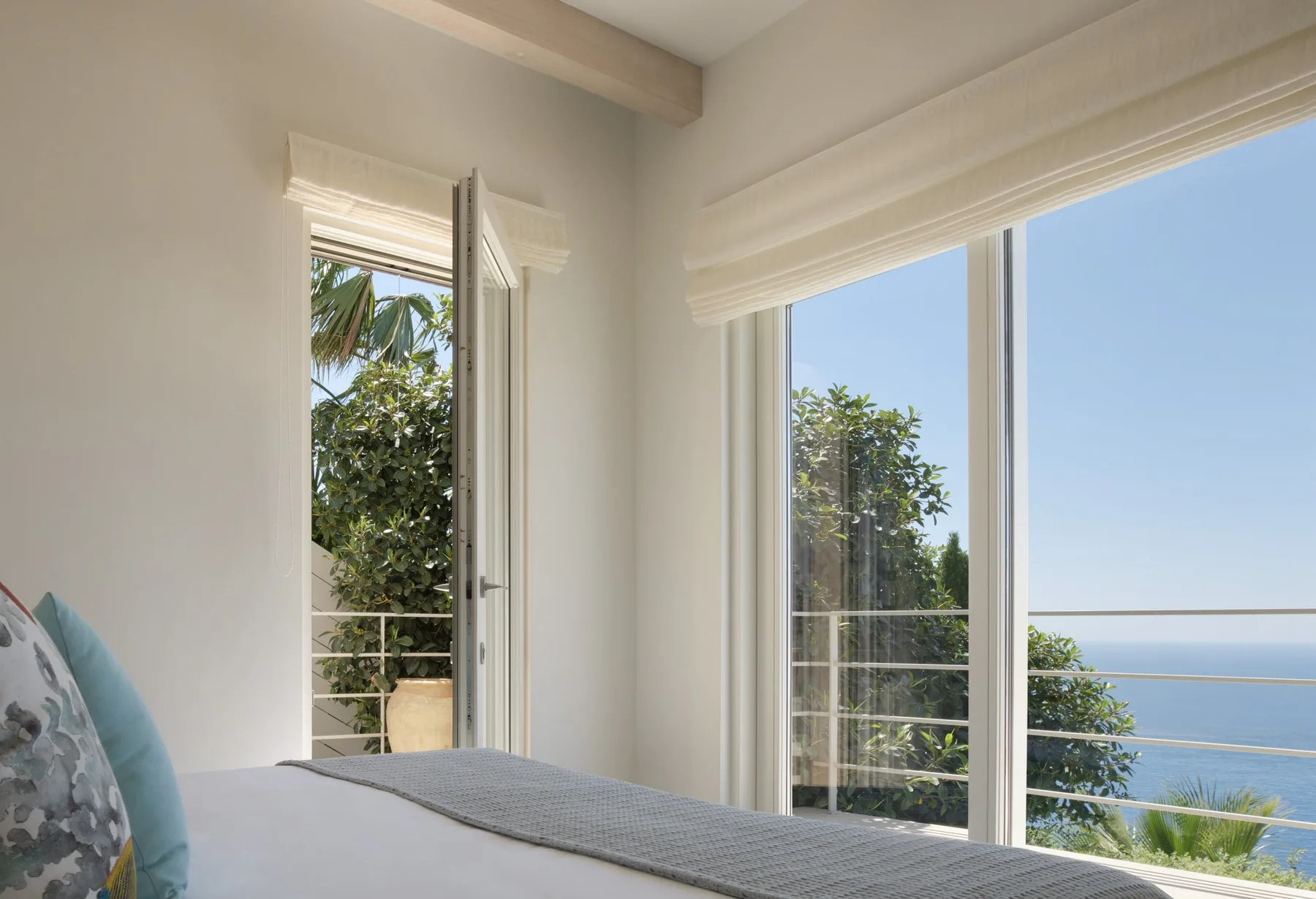 A bright bedroom with large windows overlooking trees and the sea.