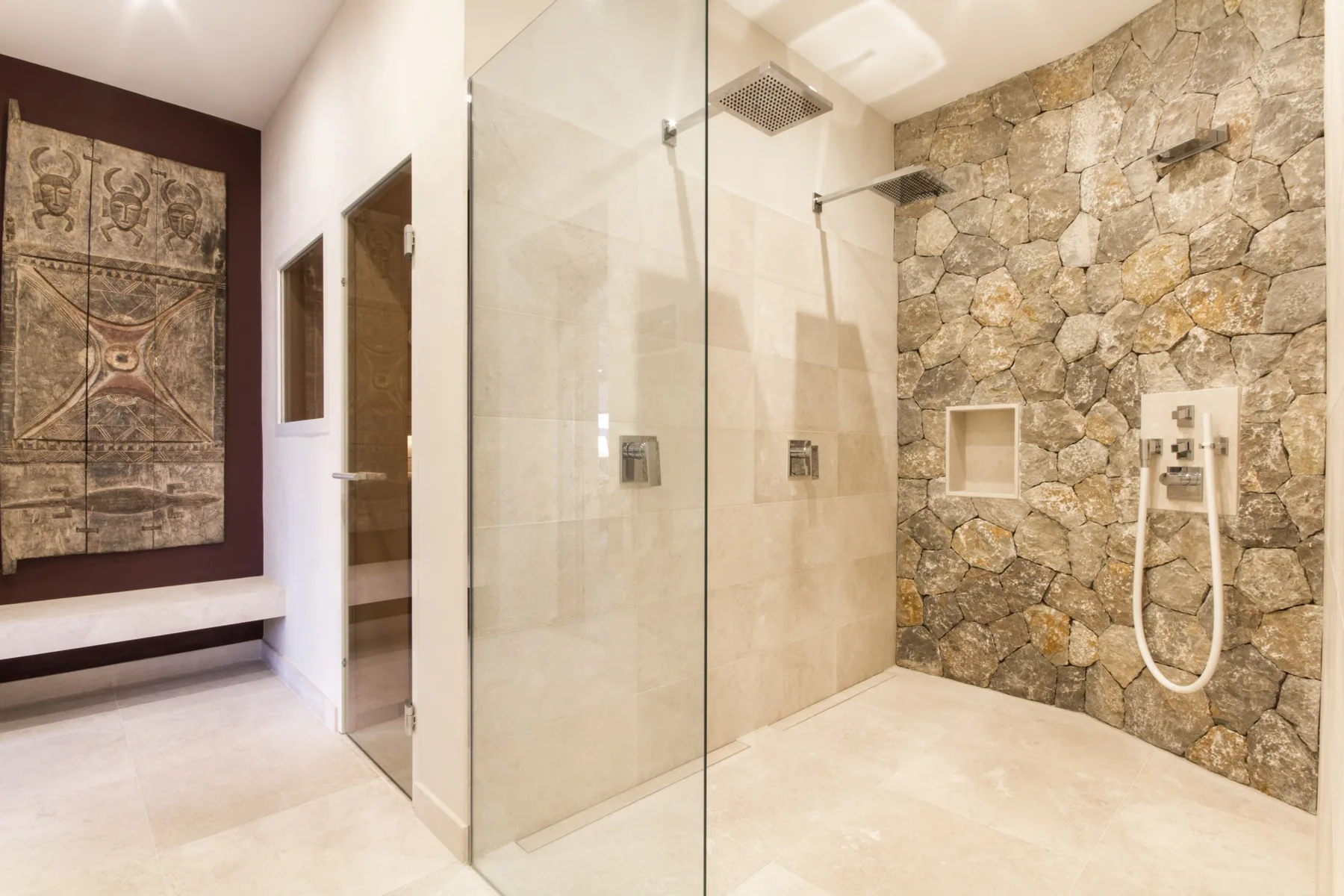 A spacious shower area with glass panels and a stone wall.