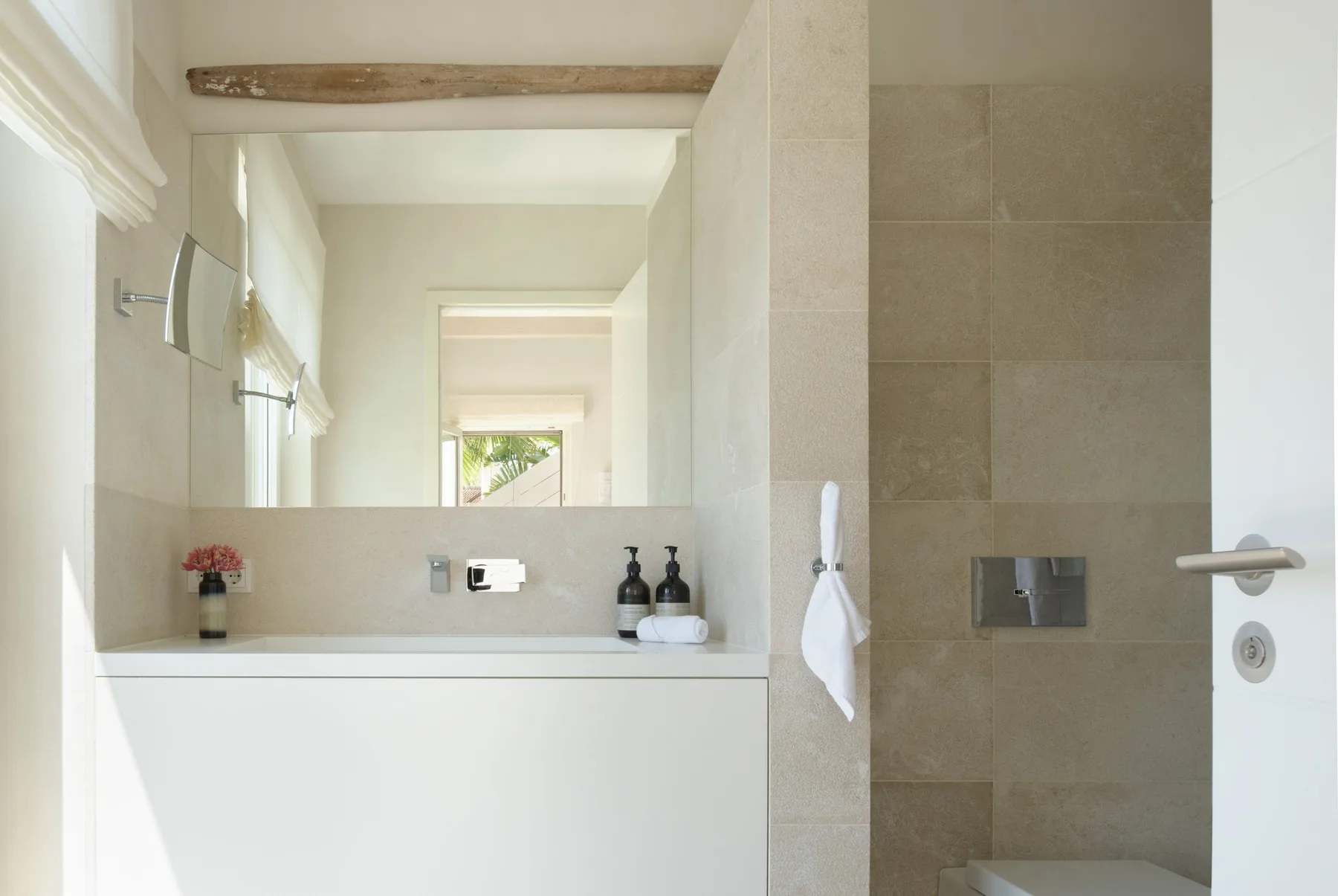 A bright bathroom with a wide mirror above the sink and a tiled shower area.
