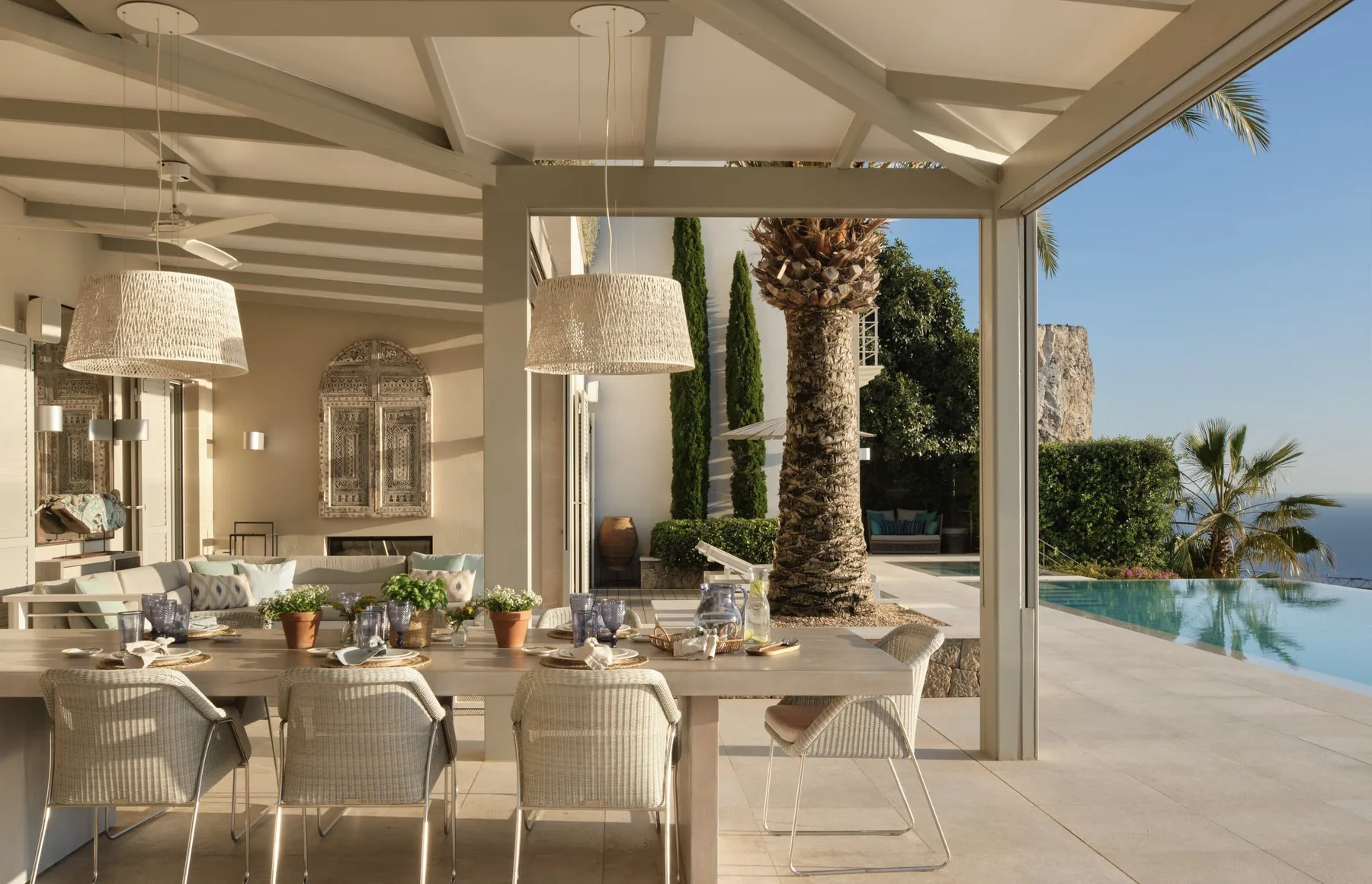 A covered outdoor dining area opens onto a pool and palm trees.