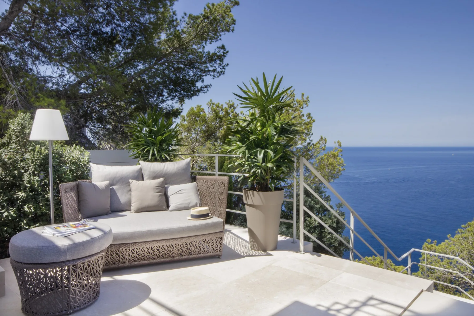 An outdoor terrace overlooks the sea, with cushioned seating and potted greenery.