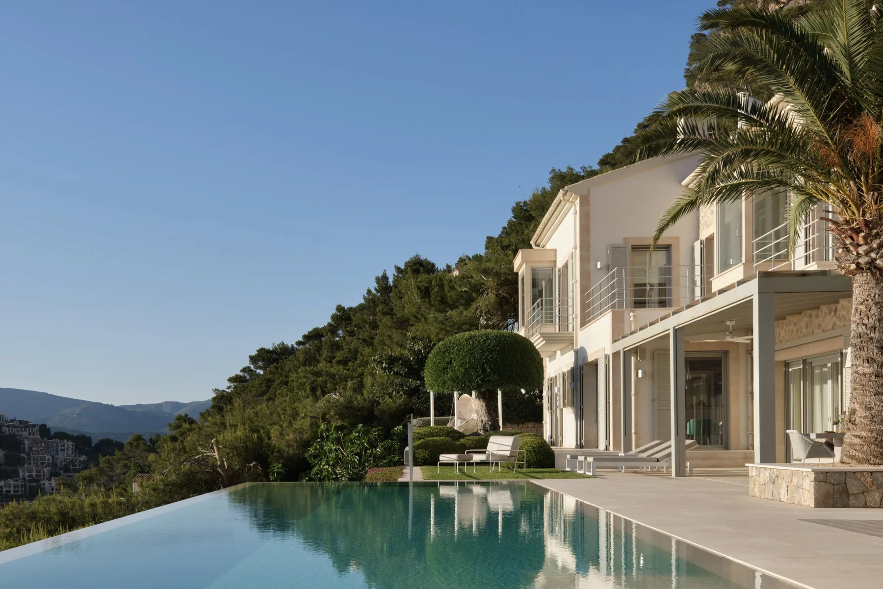 A modern house stands beside a swimming pool, with wooded hills in the background.