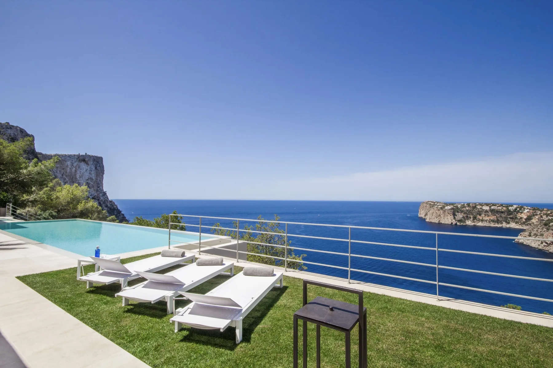 A seaside terrace has lounge seating, a small table, and a view of the sea.