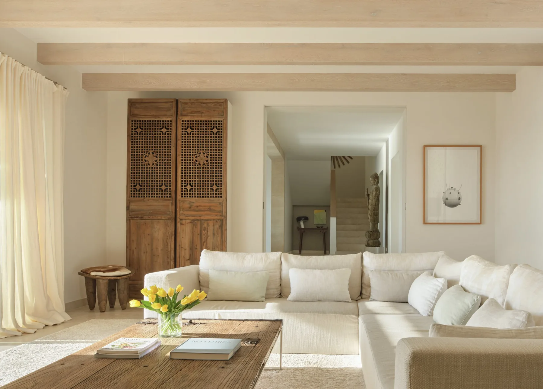 A bright living room with cream seating, a wooden coffee table, and sheer curtains.