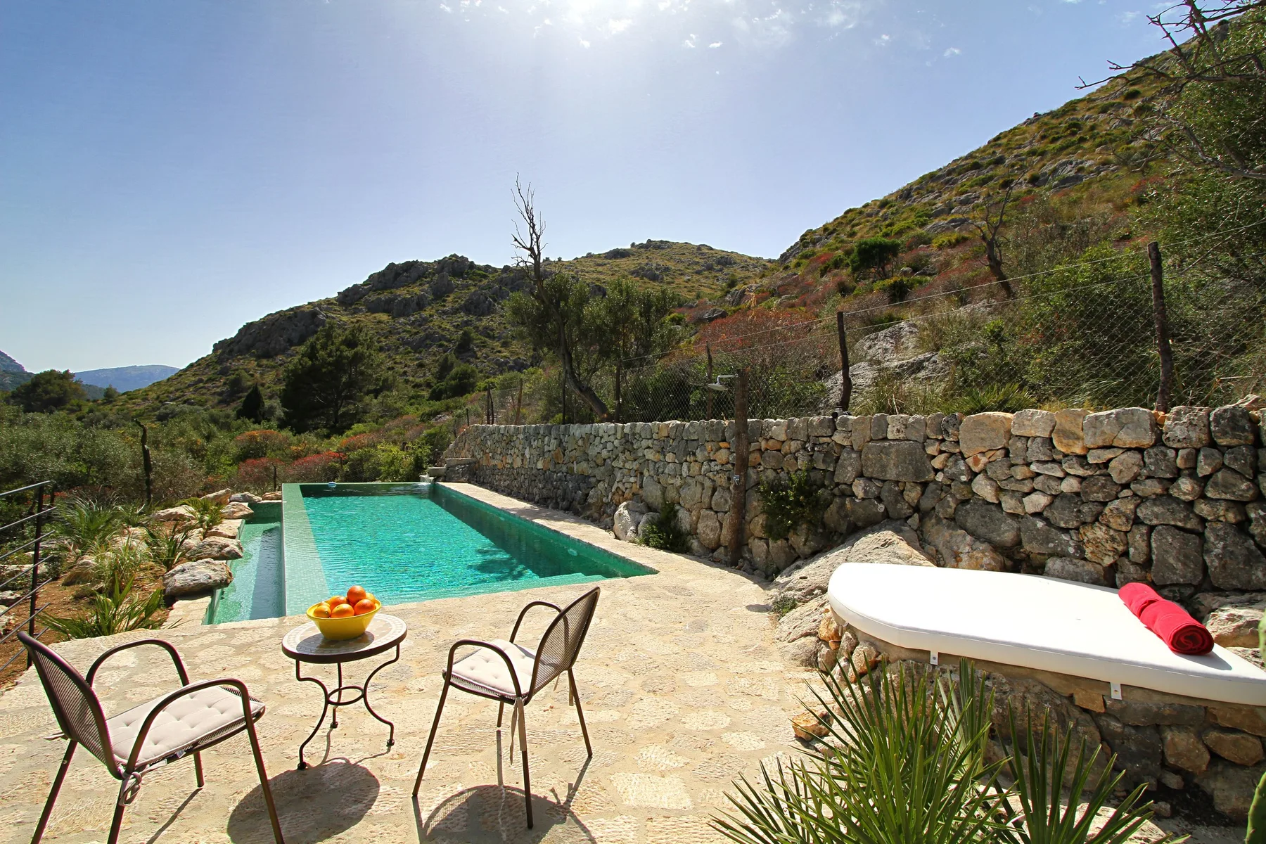 Una piscina al aire libre junto a un muro de piedra, con asientos cerca.