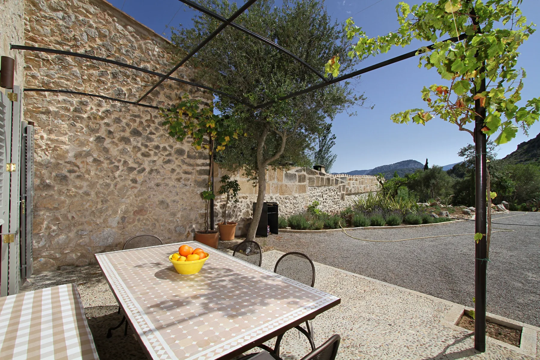 Un patio al aire libre con una mesa de comedor bajo una pérgola con hojas.