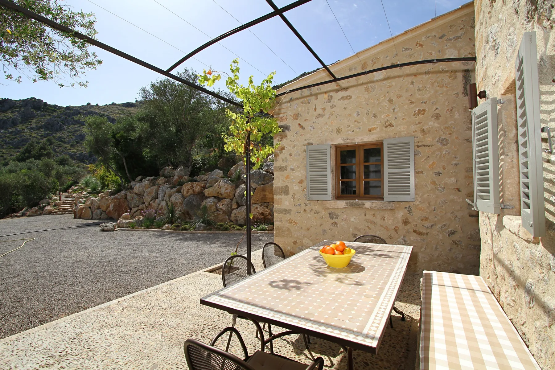 Patio de una casa de piedra con una mesa al aire libre bajo una estructura de toldo.