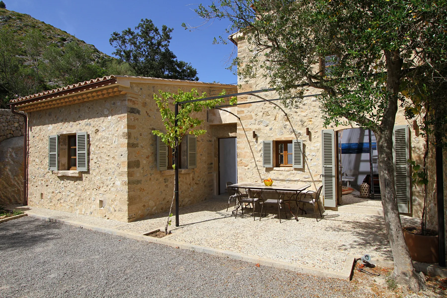Exterior de una casa de piedra con patio de grava y mesa de comedor al aire libre.