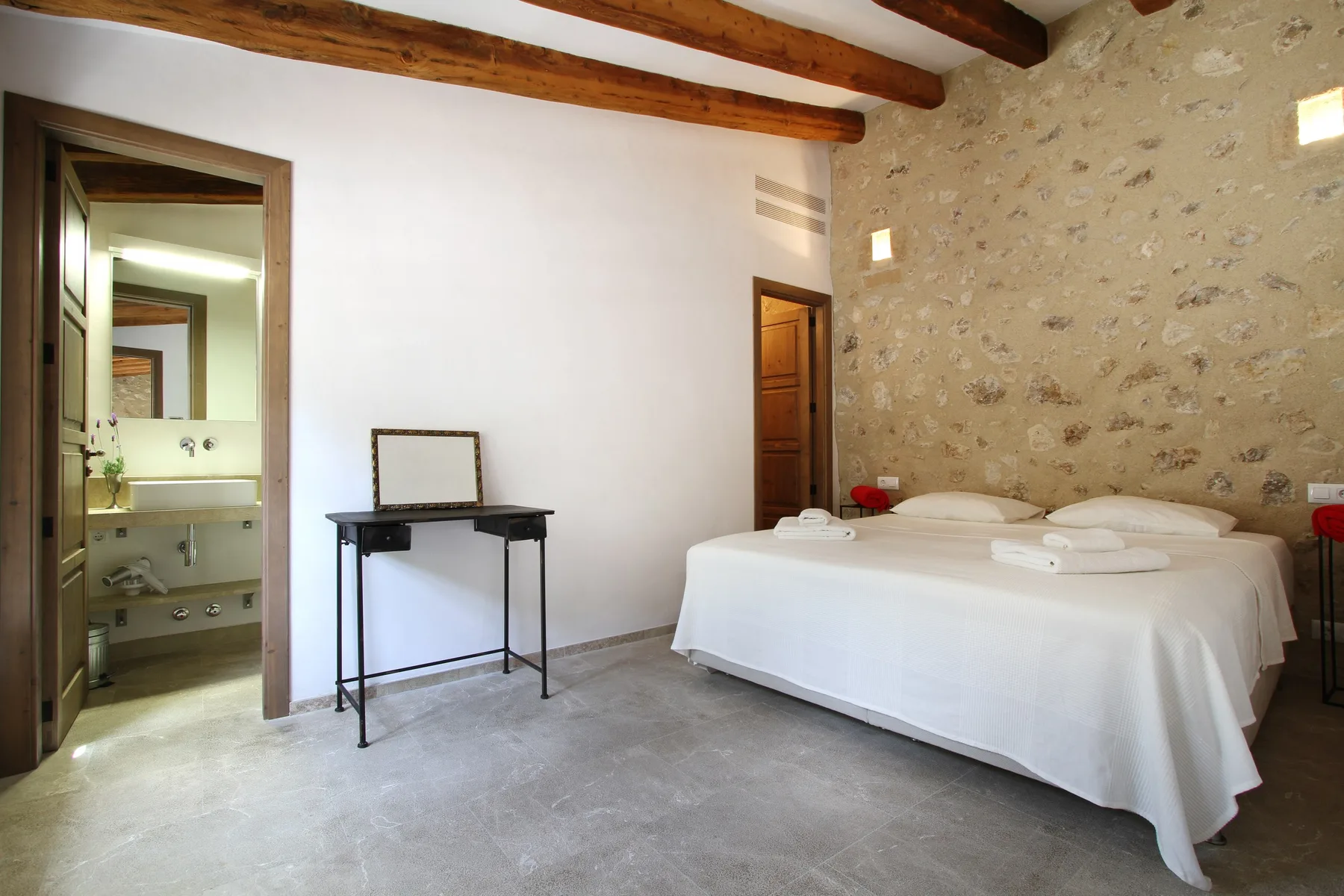Un dormitorio con una cama blanca junto a una pared de textura pétrea.