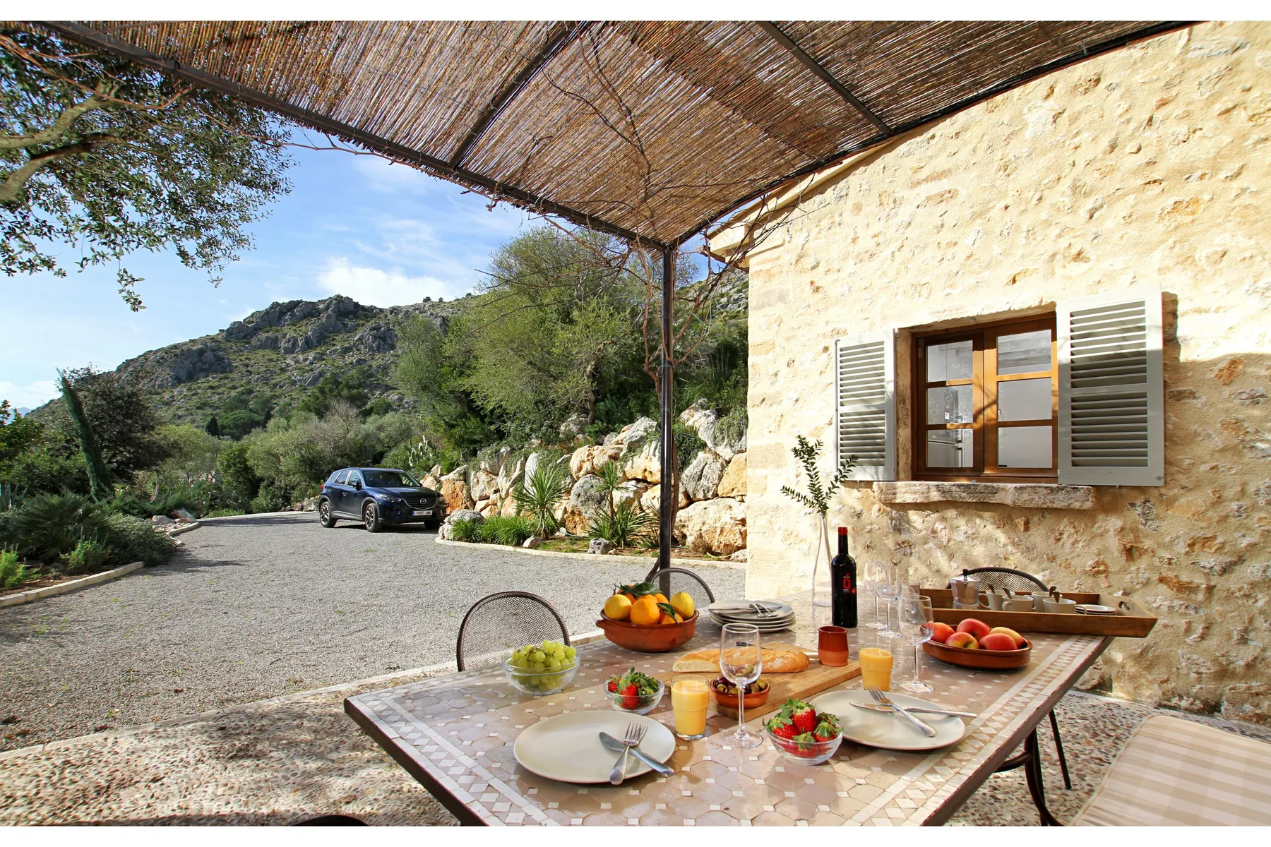 Una zona de comedor al aire libre bajo un toldo tejido, junto a una casa de piedra.