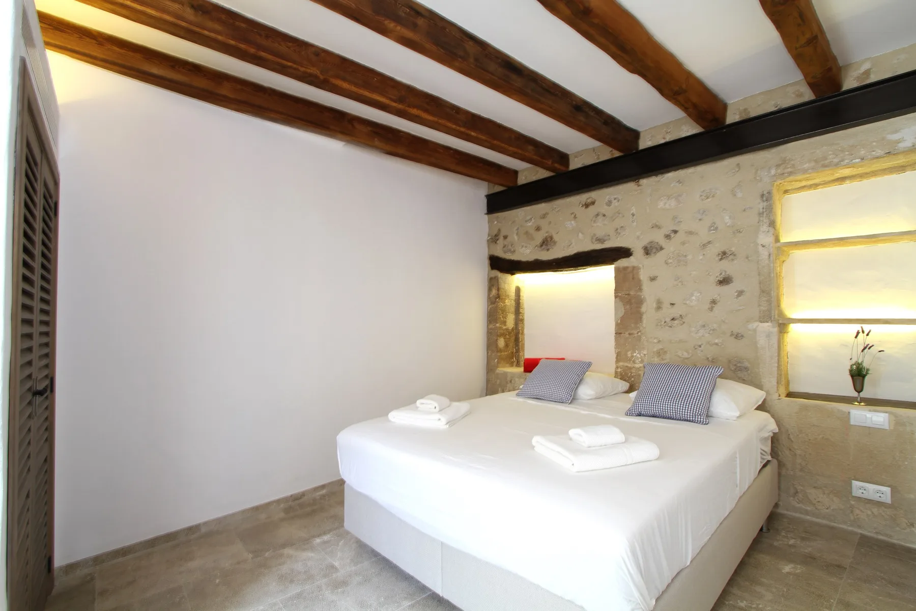 Un dormitorio con una cama doble, vigas de madera a la vista y una pared de piedra.