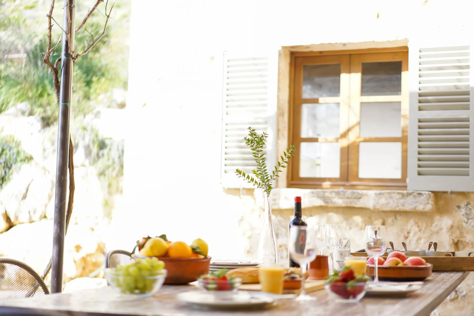 Una mesa de comedor al aire libre está servida con fruta bajo una ventana.