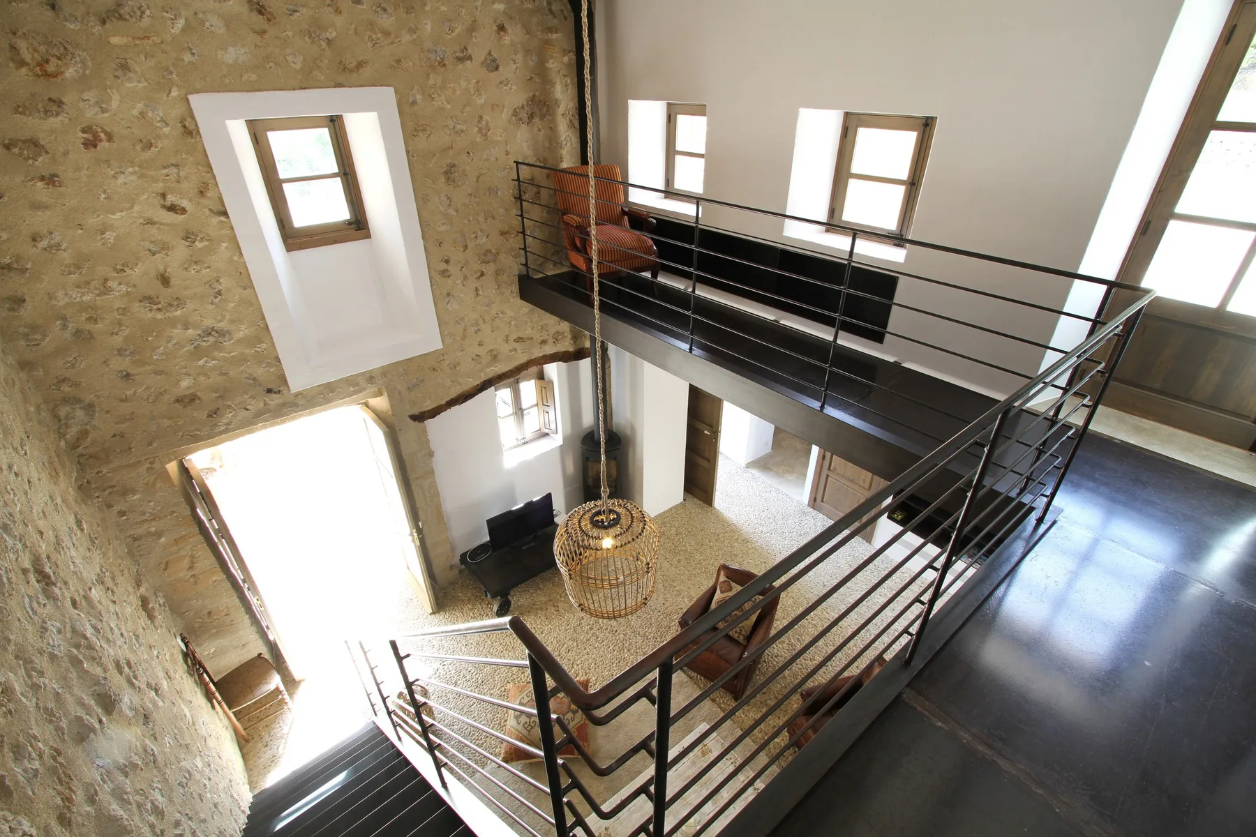 Interior tipo loft con una entreplanta de barandilla metálica sobre una sala de estar.