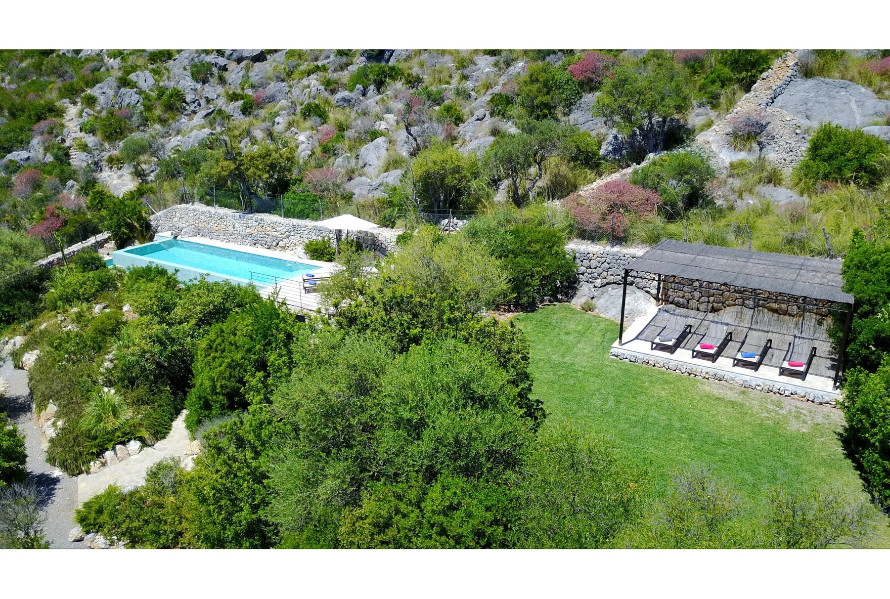 Una piscina al aire libre y una zona de asientos con sombra están junto a un césped verde.