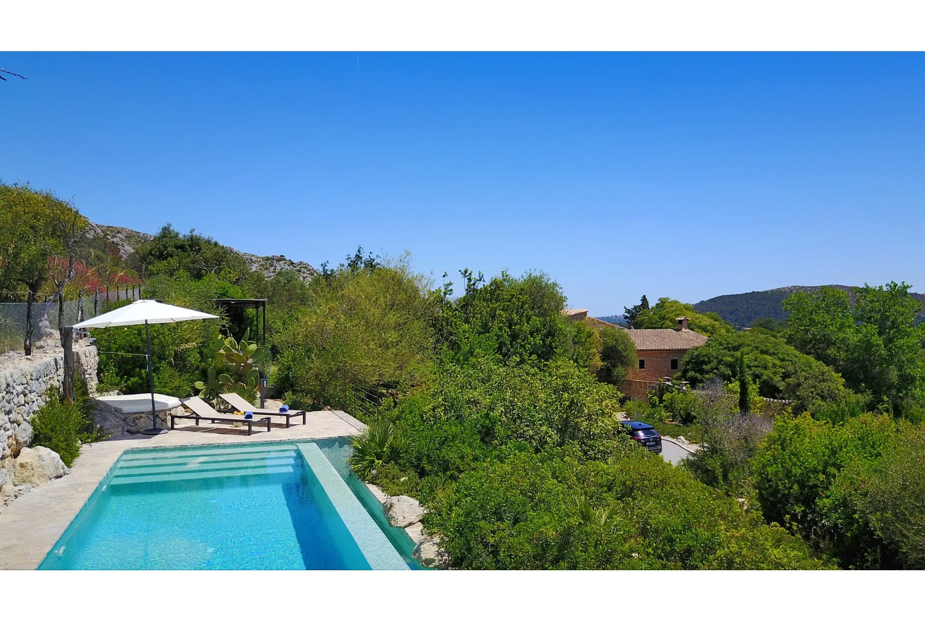 Piscina al aire libre junto a un jardín, con colinas visibles a lo lejos.