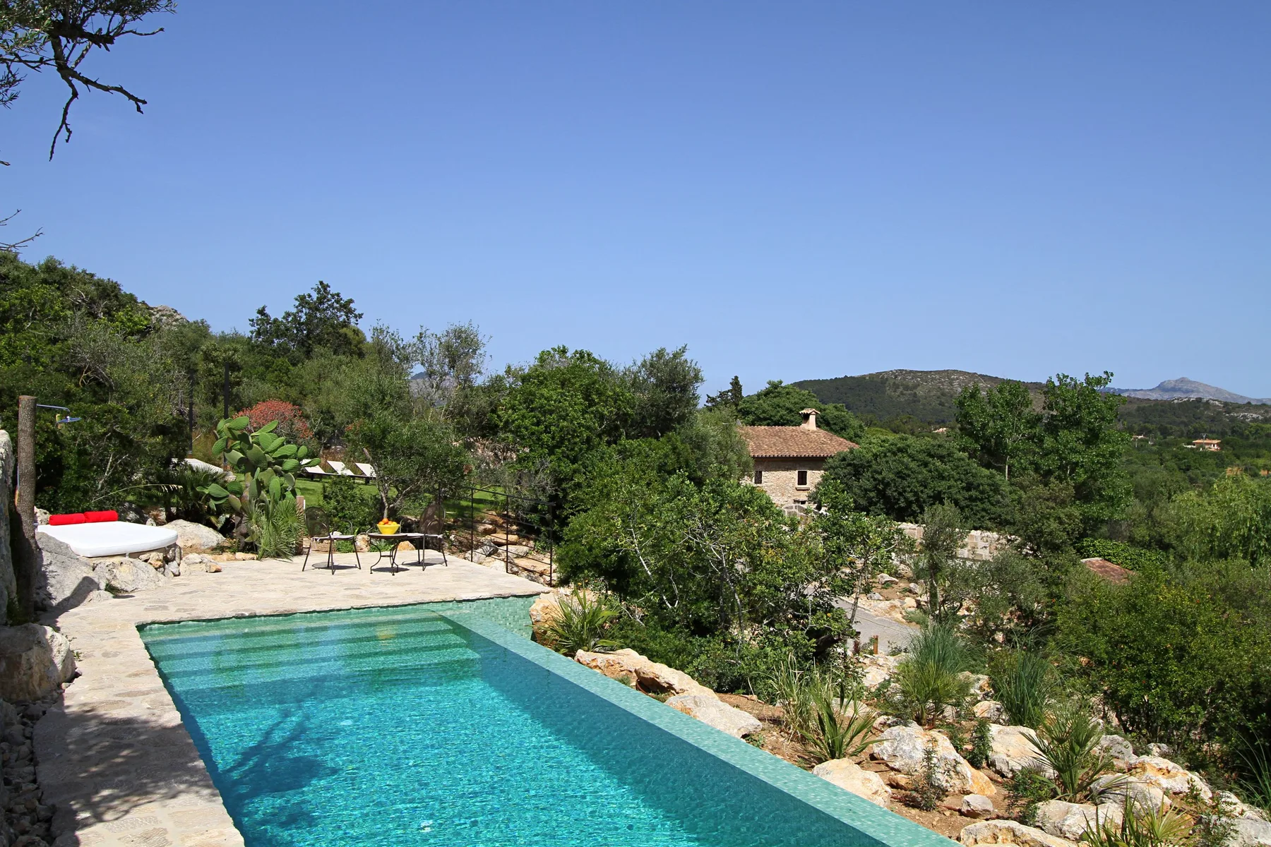 Una piscina al aire libre está rodeada de vegetación, con colinas a lo lejos.