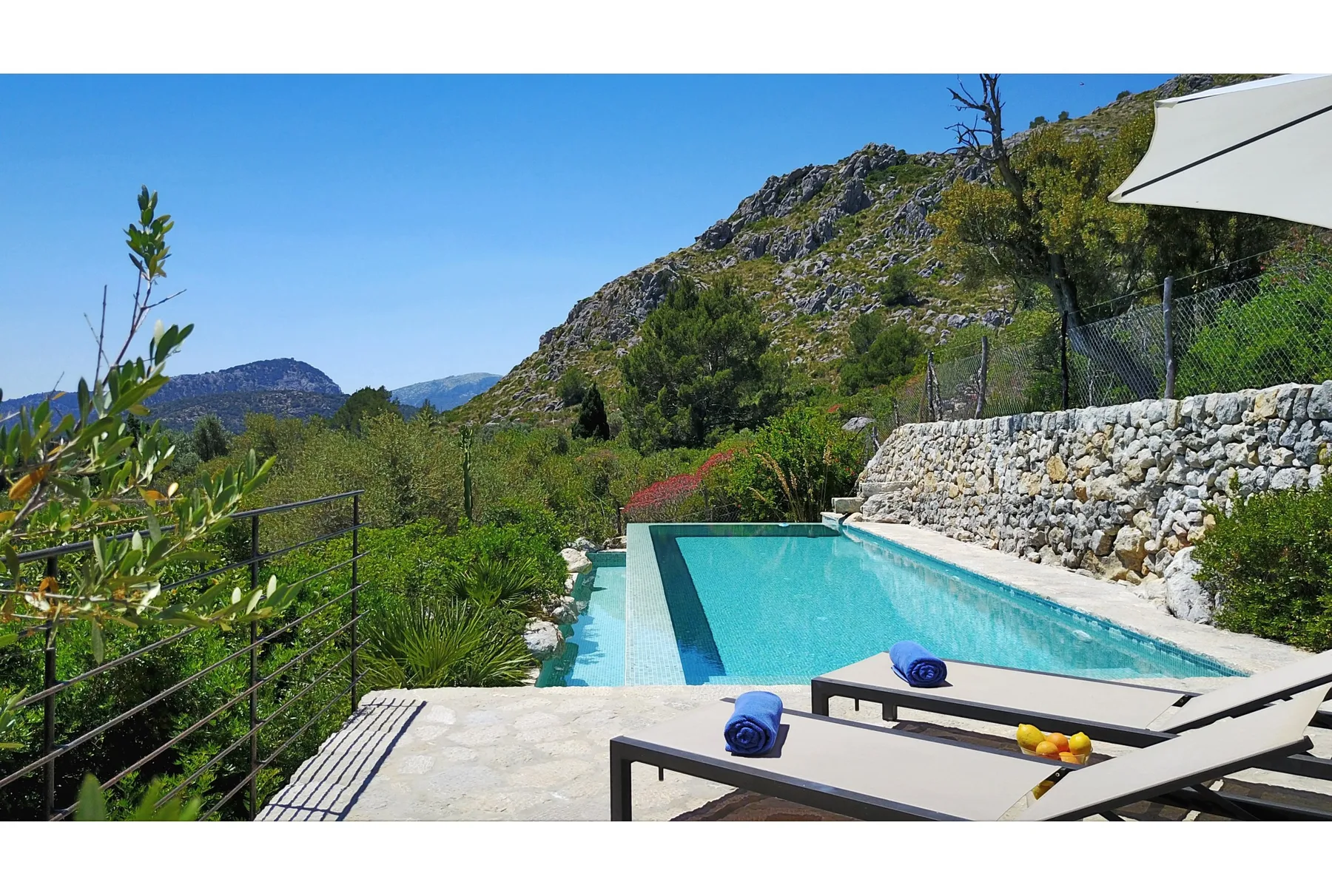 Una piscina al aire libre está junto a un muro de piedra, con colinas verdes al fondo.