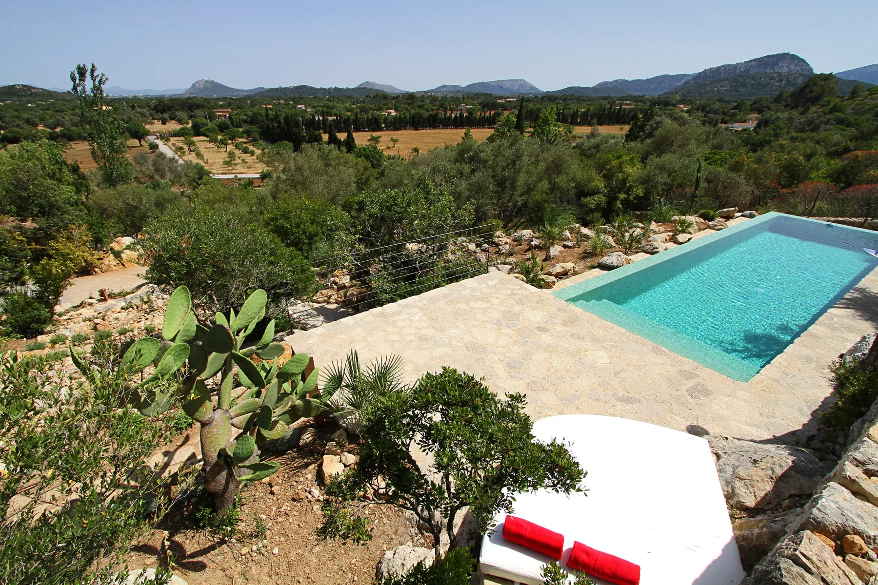 Una piscina exterior junto a un patio de piedra clara, con colinas verdes a lo lejos.