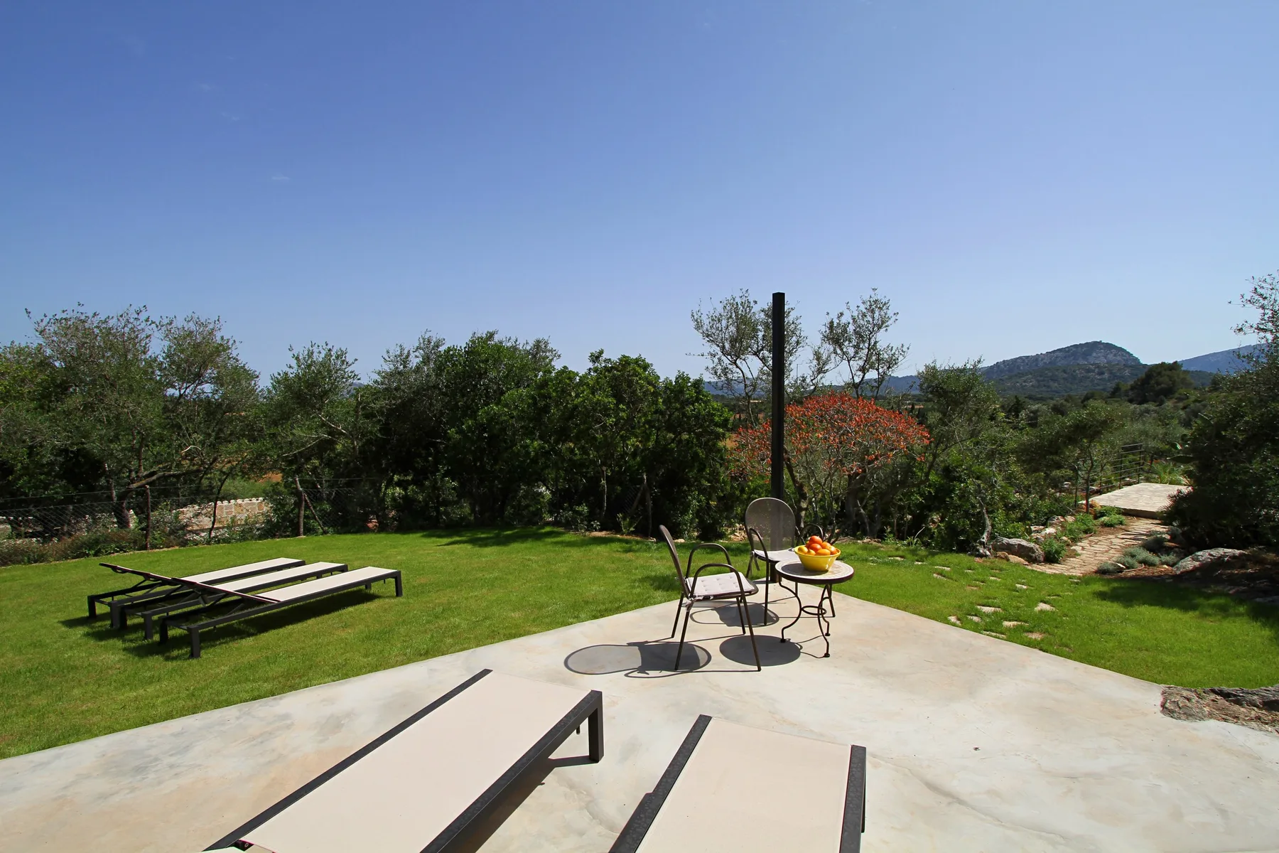 Un patio al aire libre con asientos de descanso da a un jardín verde y colinas lejanas.