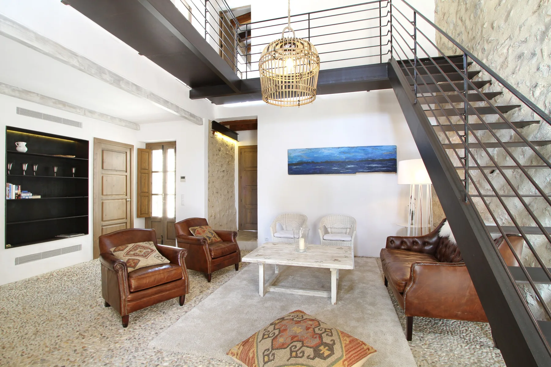 Una sala de estar con asientos, una mesa de centro y una escalera hacia un nivel superior.