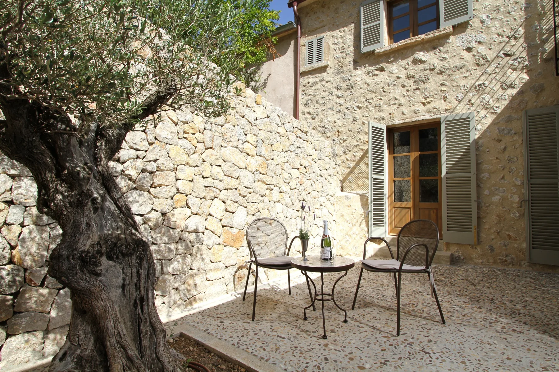 Un patio de piedra con una mesa pequeña y sillas junto a un árbol.