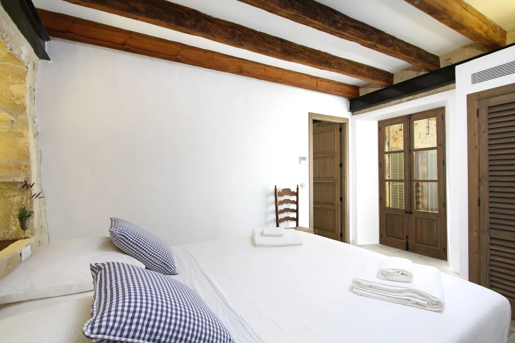 Un dormitorio con una cama blanca, almohadas estampadas y vigas de madera a la vista.