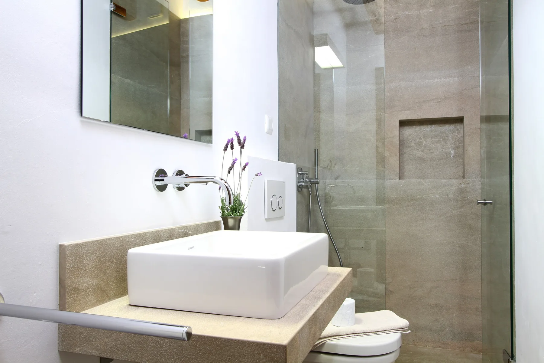 Un baño moderno con un lavabo rectangular junto a una ducha con mampara de vidrio.