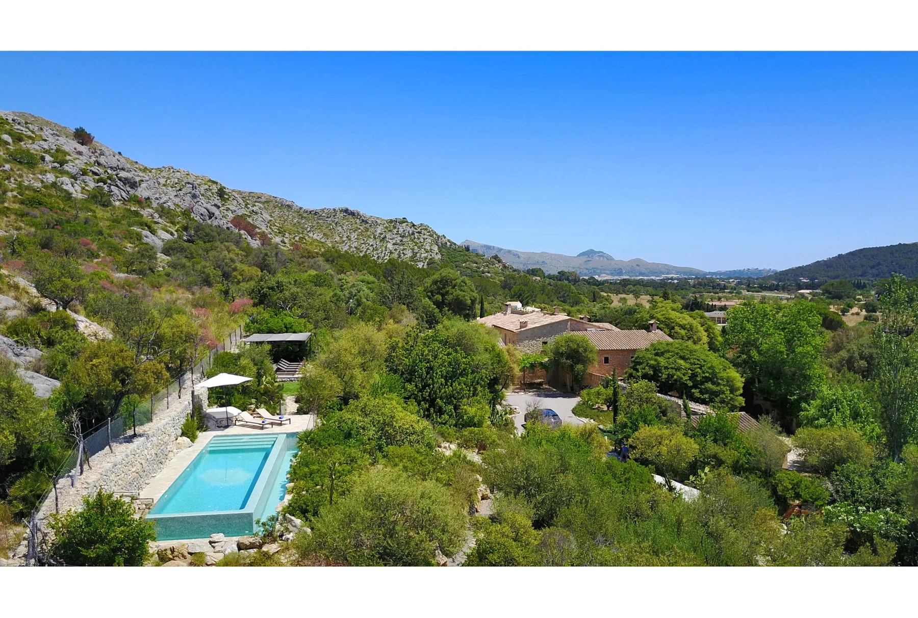 Una piscina está rodeada de colinas verdes y edificios dispersos bajo un cielo azul despejado.