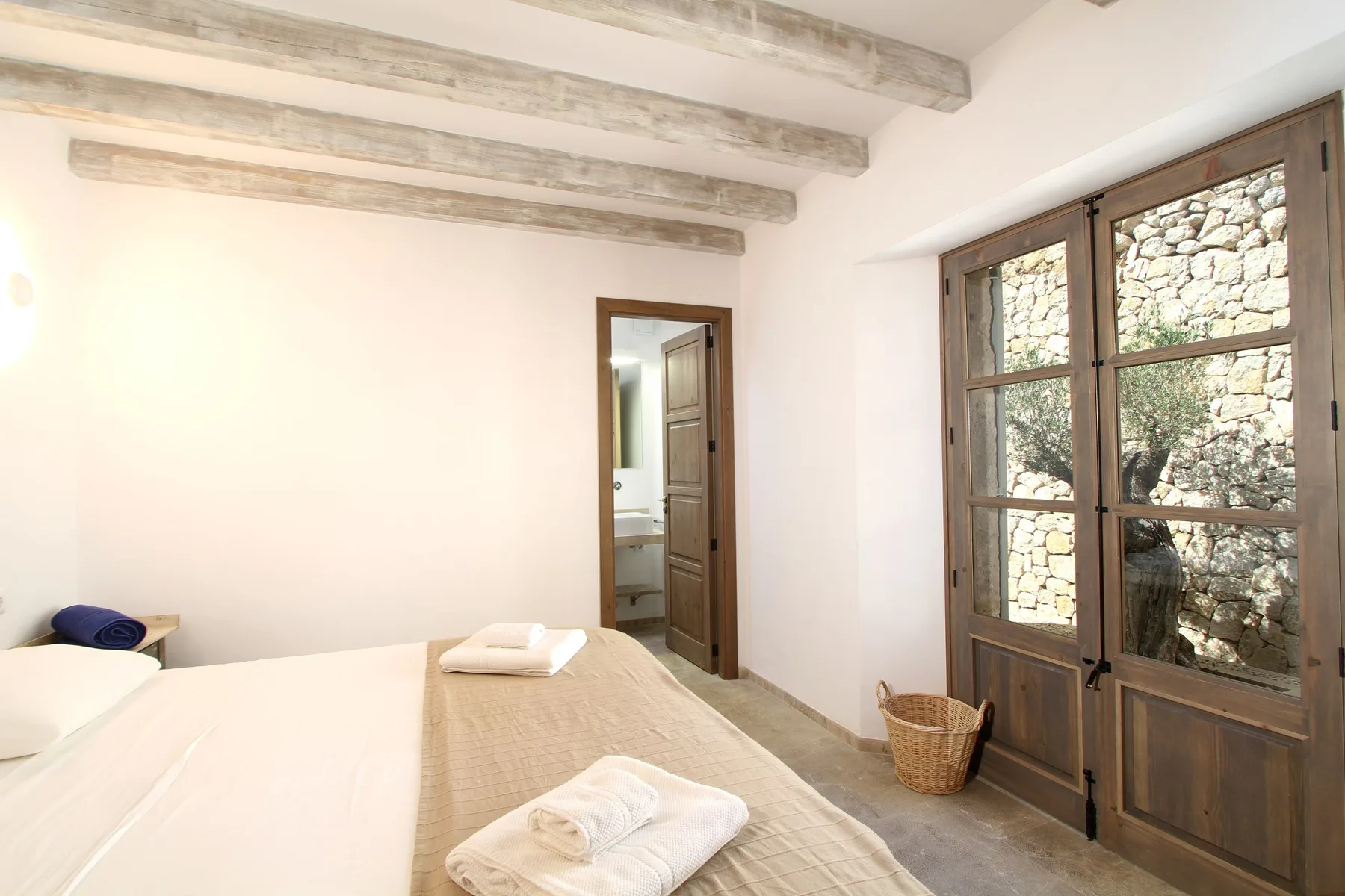 Un dormitorio luminoso con una cama junto a ventanas altas de madera.
