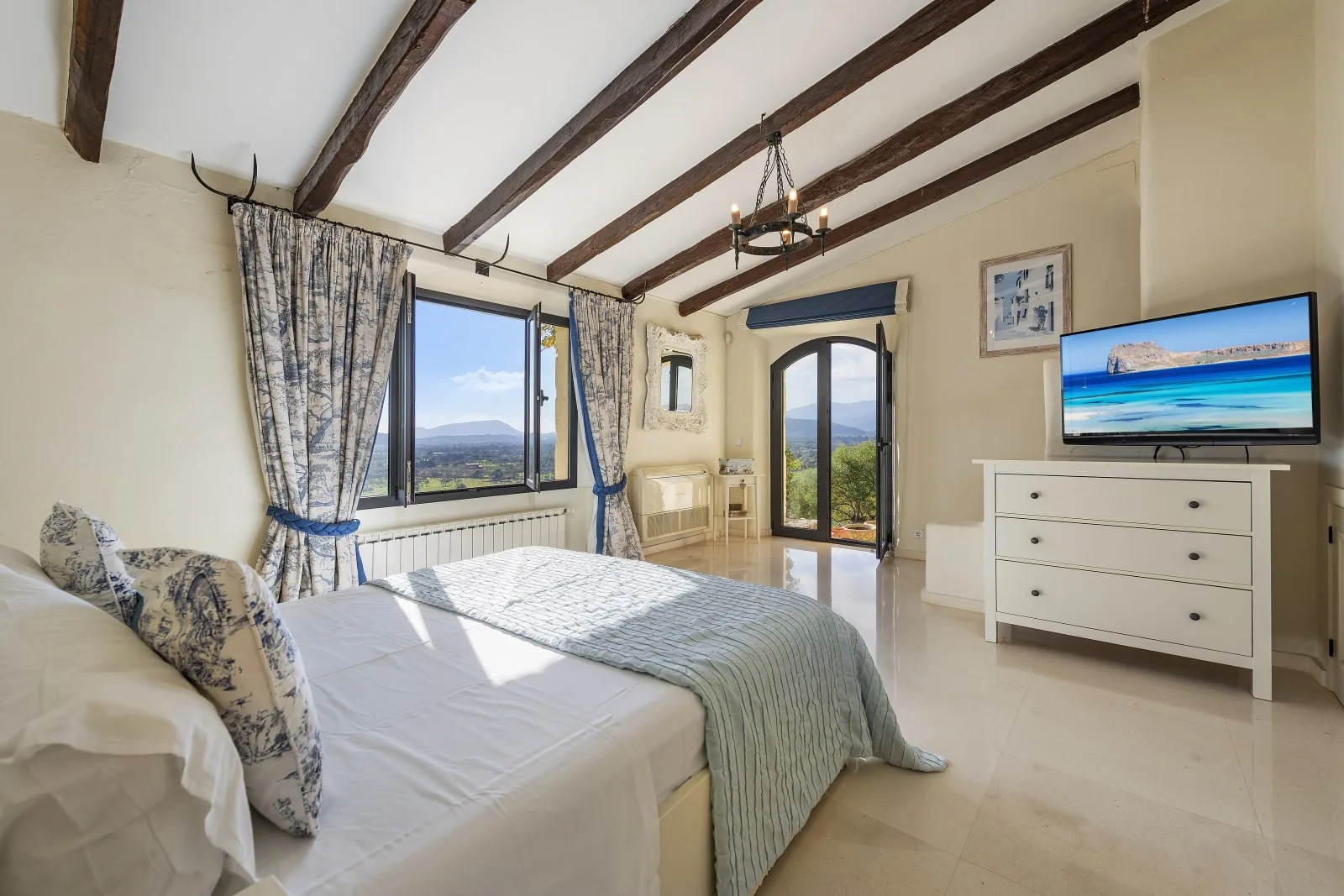A bedroom with a bed, large windows, and a television on a dresser.