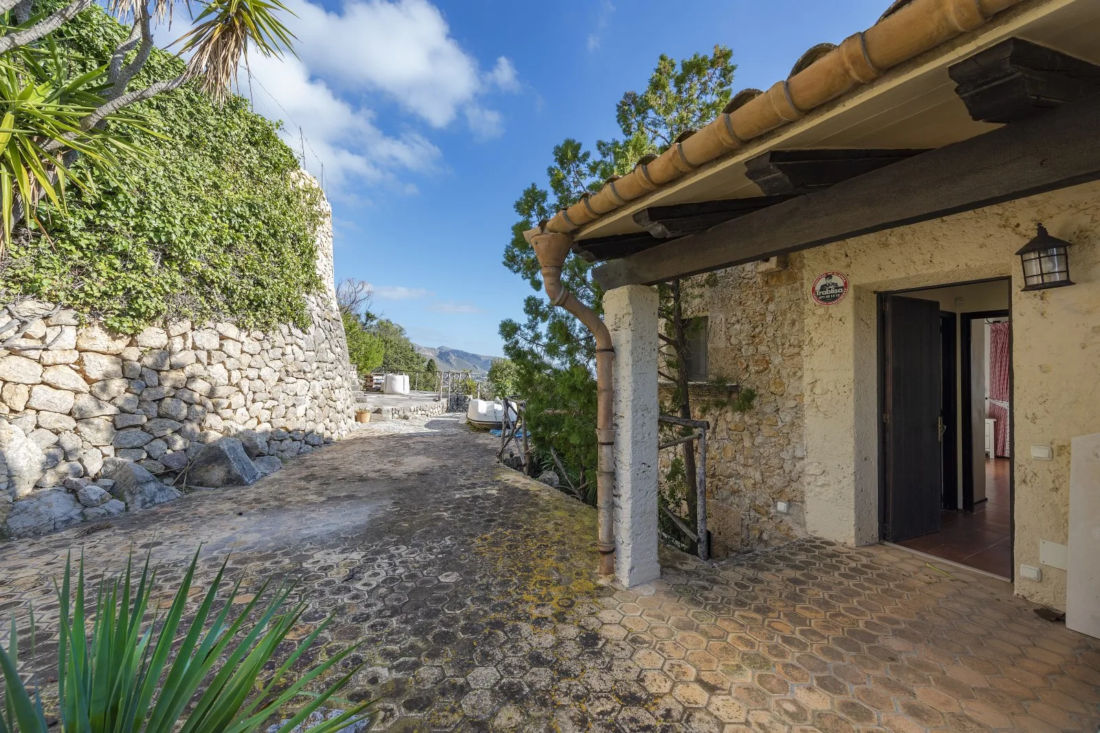 A stone-paved courtyard path runs beside a rustic stone building under a clear blue sky.