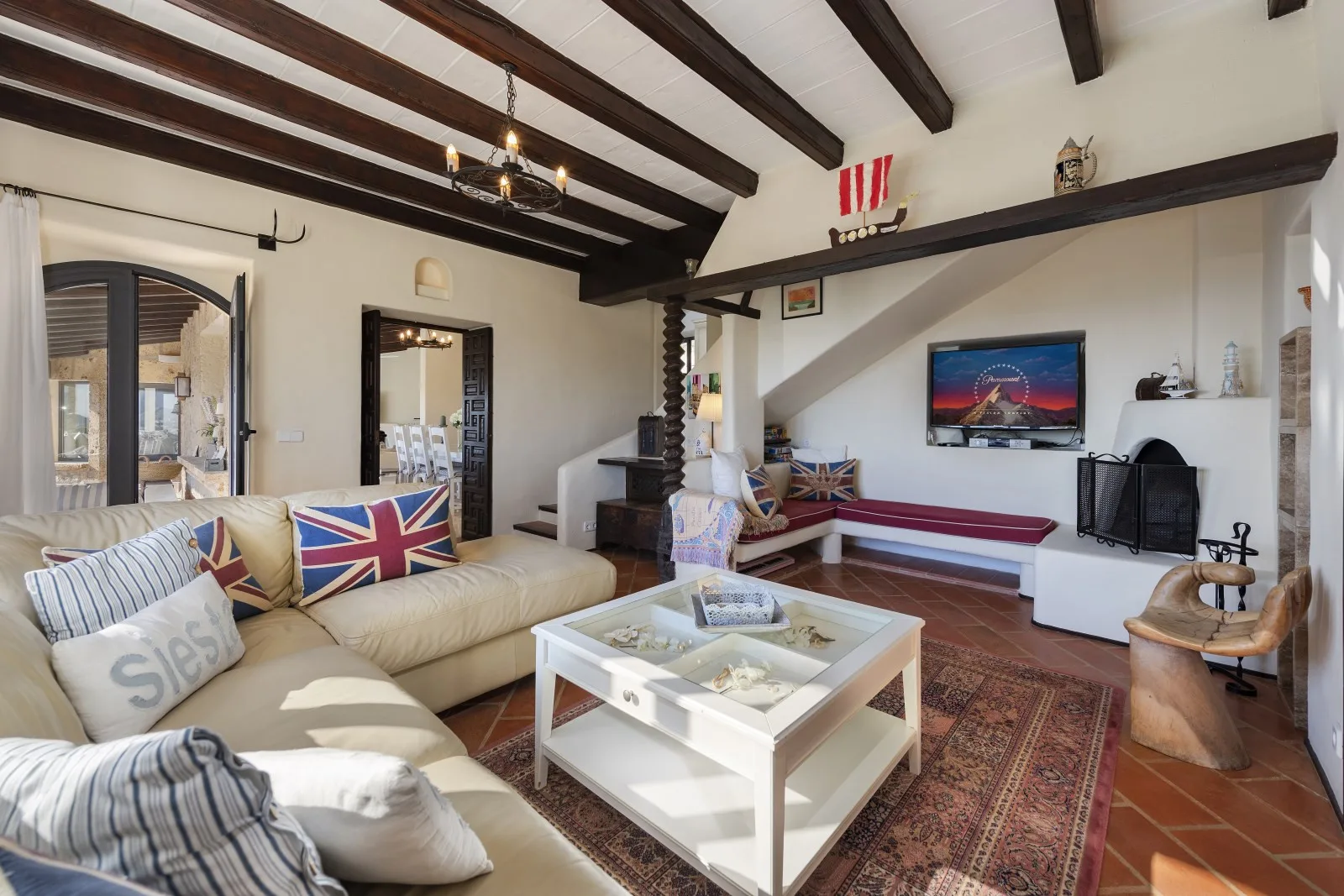 A bright living room with seating, a coffee table, and a television beneath exposed ceiling beams.