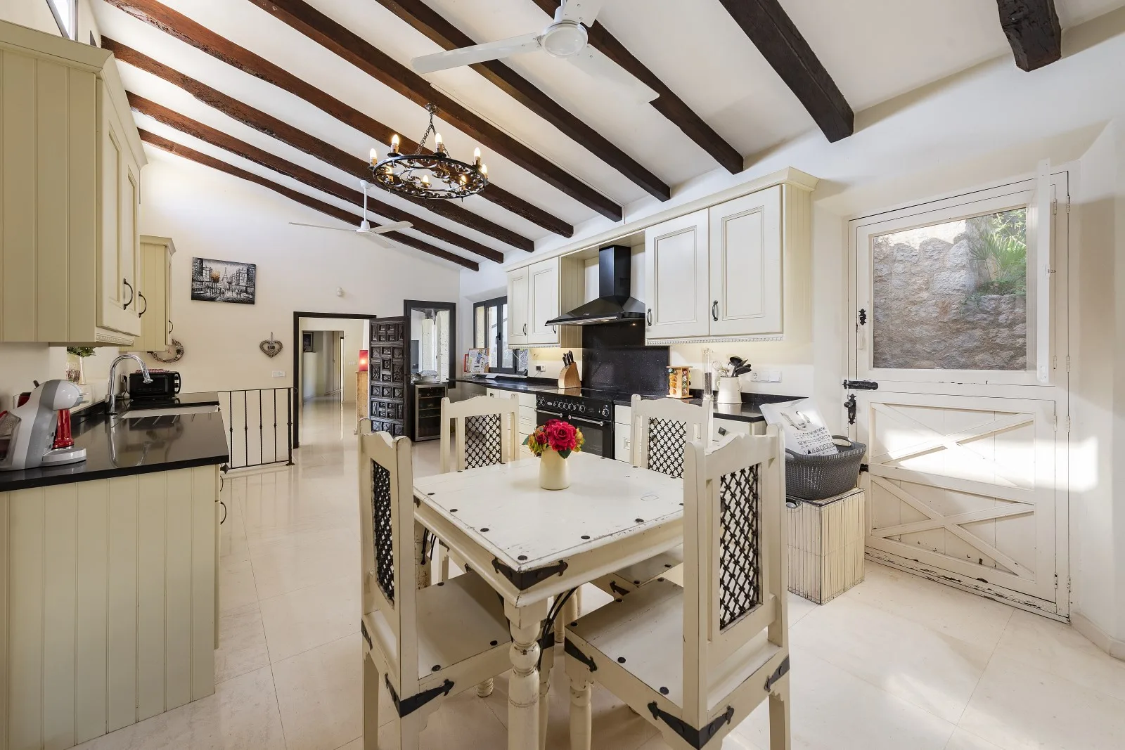 A bright kitchen and dining area with a long table and exposed ceiling beams.