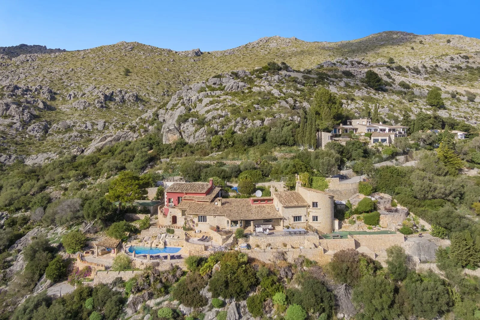 A hillside property sits among rocky slopes and greenery, with a pool nearby.