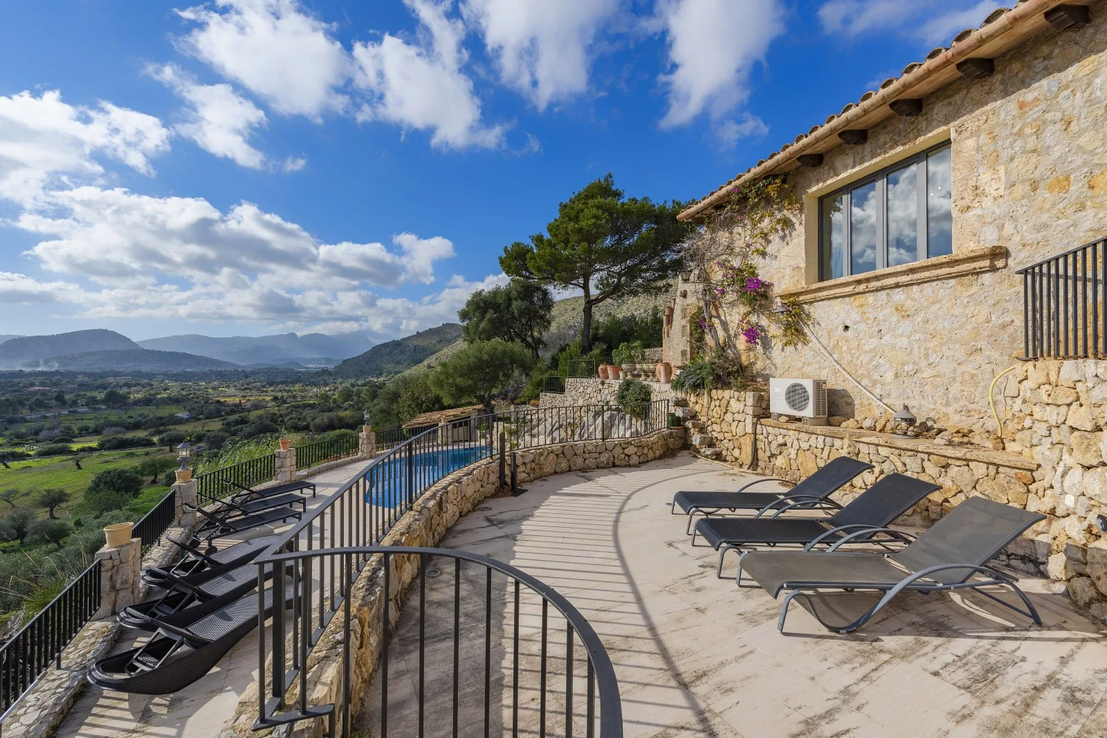 A stone terrace with lounge seating overlooks a pool and a green valley.
