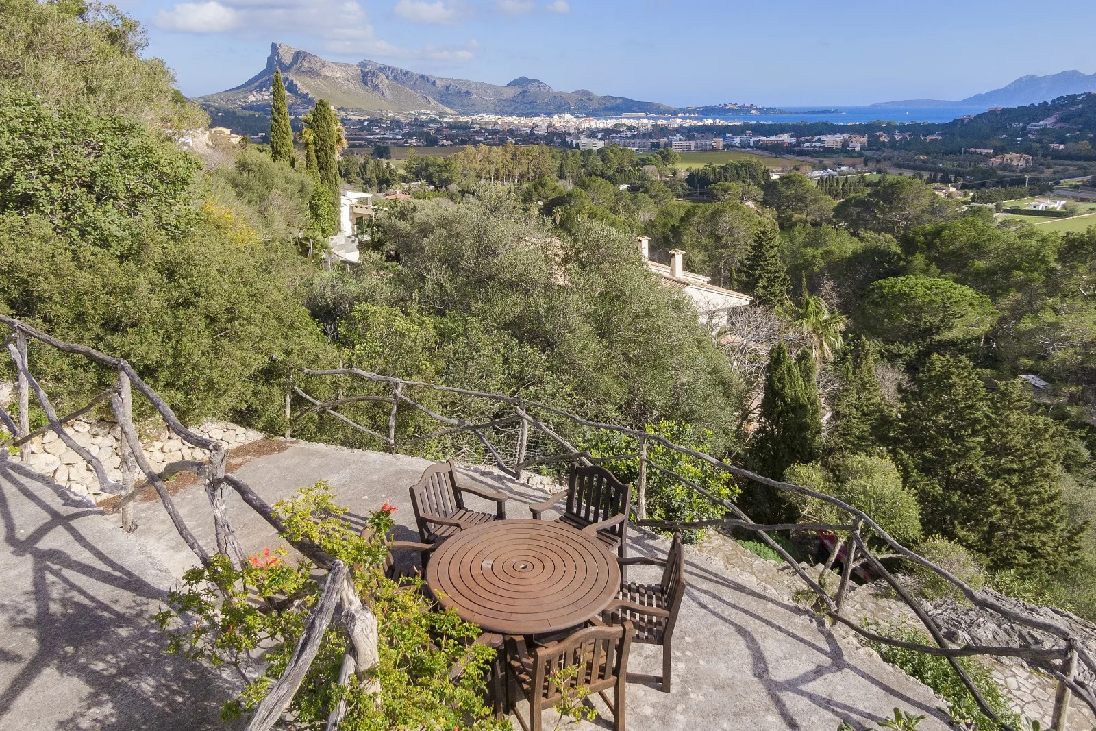 A hillside terrace with outdoor seating overlooks a green valley and distant mountains.