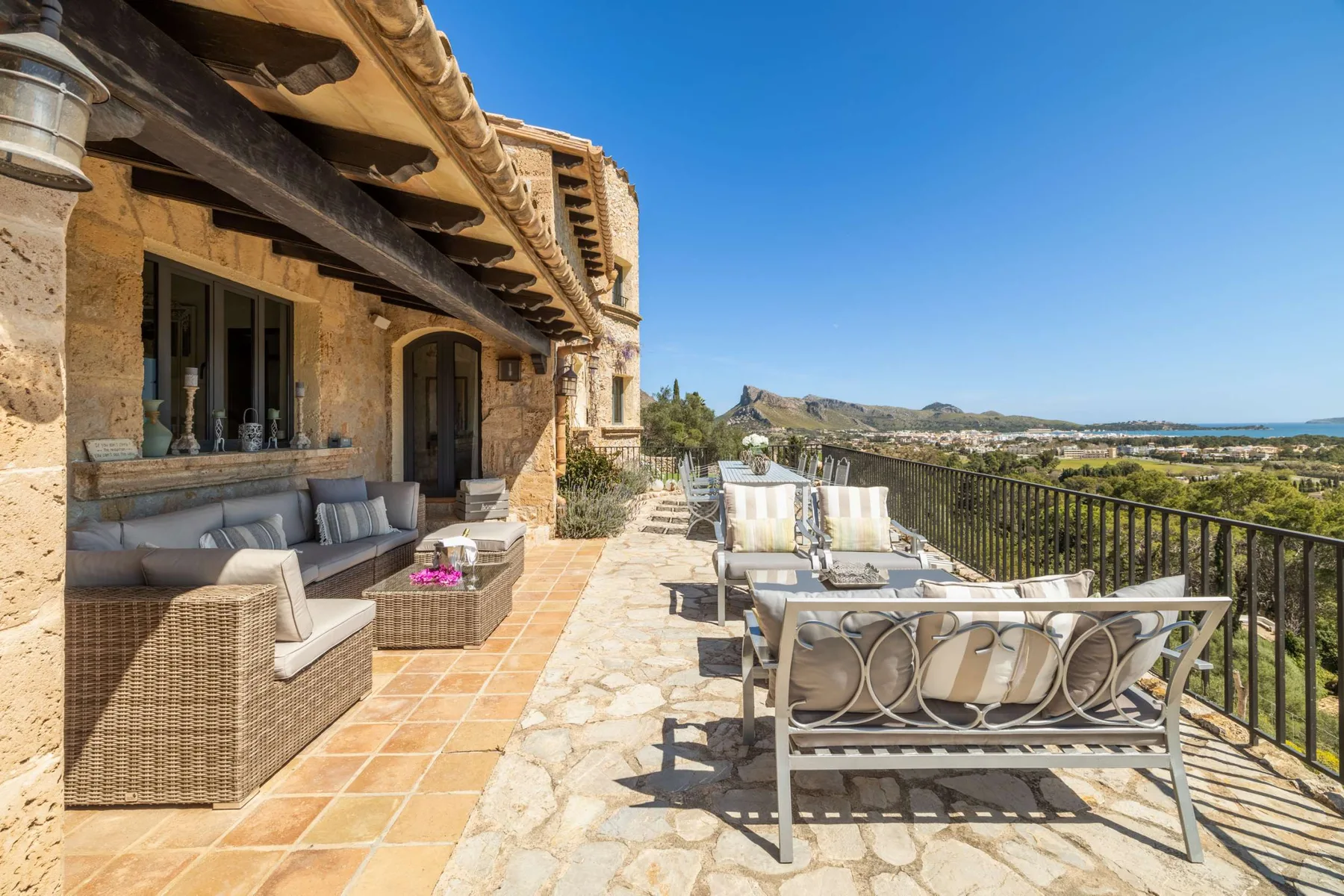 A stone terrace with outdoor seating overlooks a sunlit landscape.