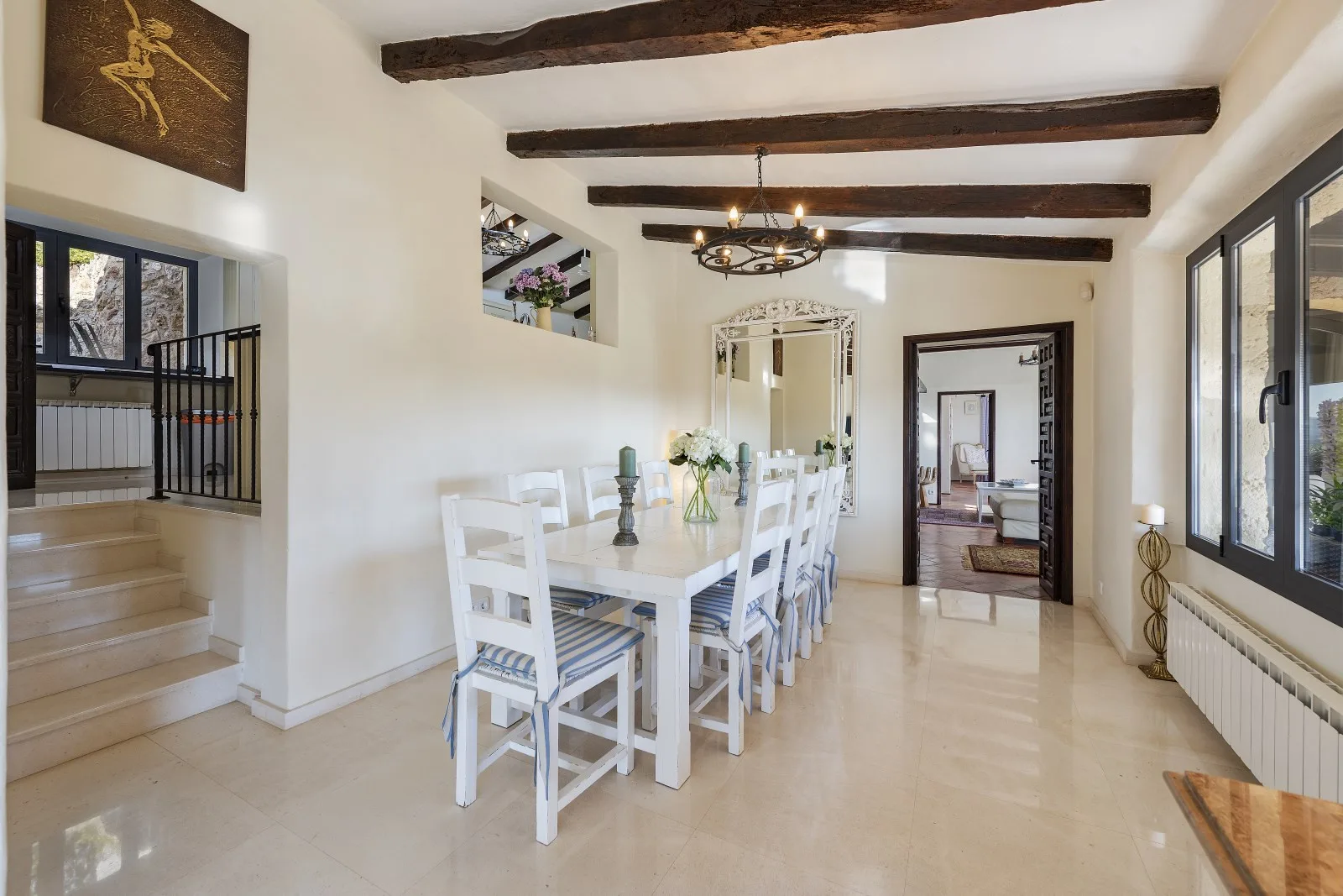 A bright dining area with a long table beneath exposed wooden ceiling beams.