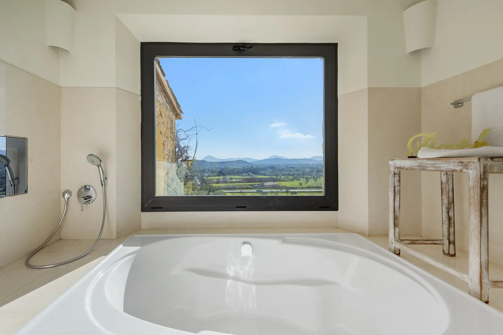 A bathroom with a large bathtub overlooking a green valley and distant hills.