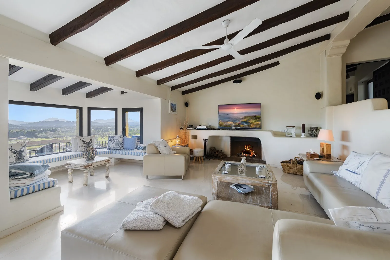 A spacious living room with seating, a fireplace, and large windows overlooking the landscape.