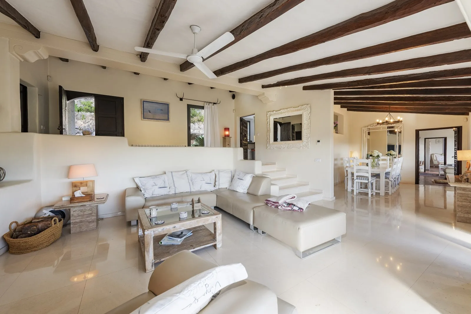 A bright living room with a seating area and dining table under exposed ceiling beams.