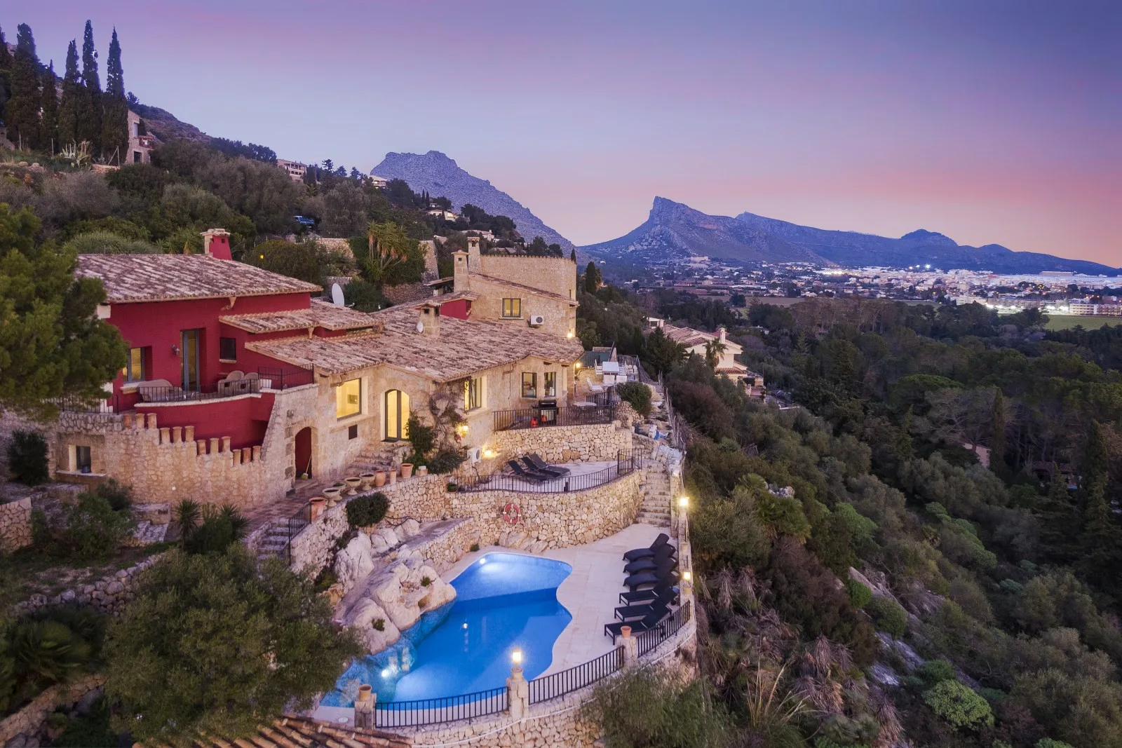 A hillside resort with a blue swimming pool overlooks a wooded valley and distant mountains.