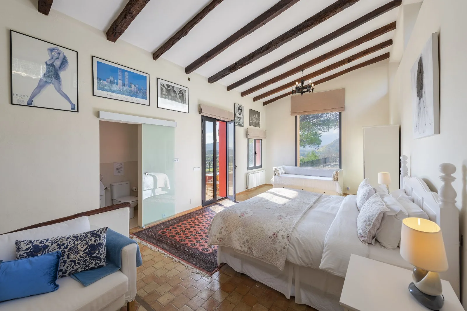 A bright bedroom with a large bed, exposed ceiling beams, and framed artwork.