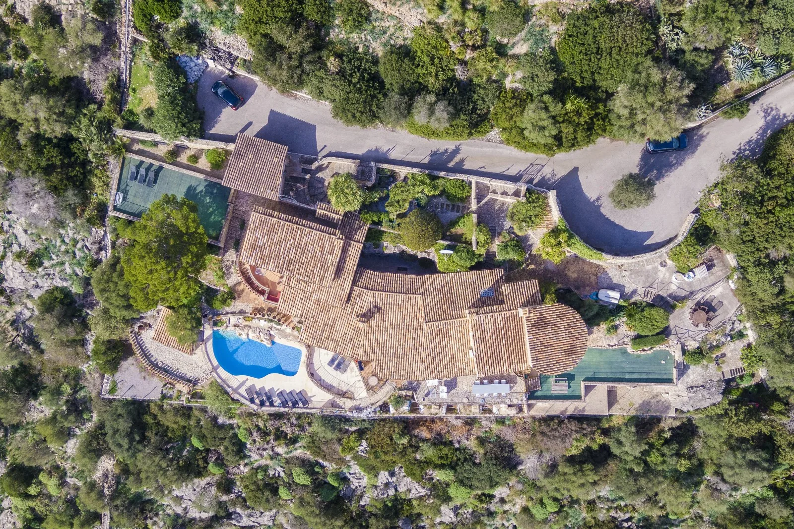 Aerial view of a large property with tiled roofs, a swimming pool, and surrounding greenery.