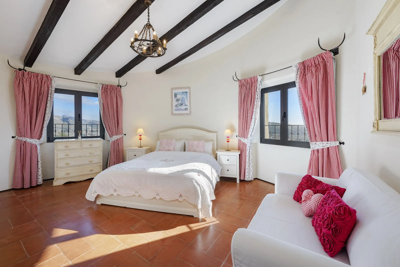 A bright bedroom with a large bed, curtained windows, and a white sofa.